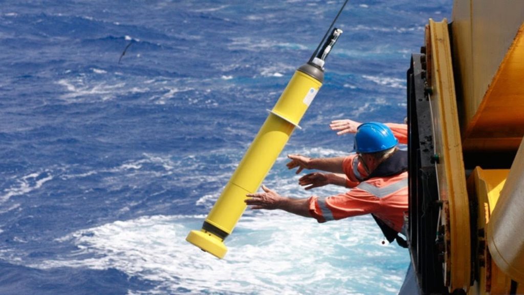 Scientists toss a yellow Argo float over the side of the ship and into the ocean.