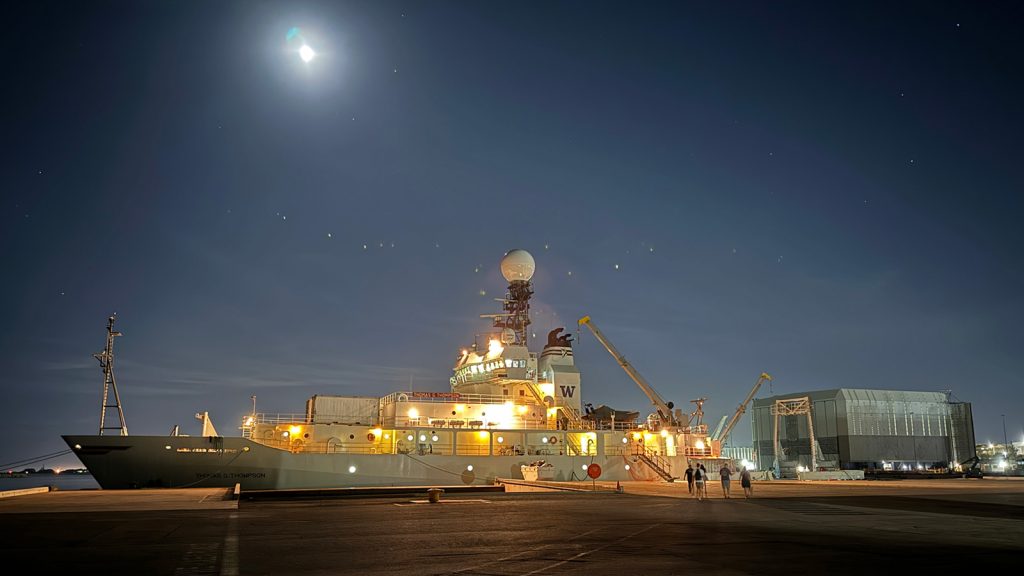 The R/V Thomas G. Thompson in port with the ship lights shining against the night sky.