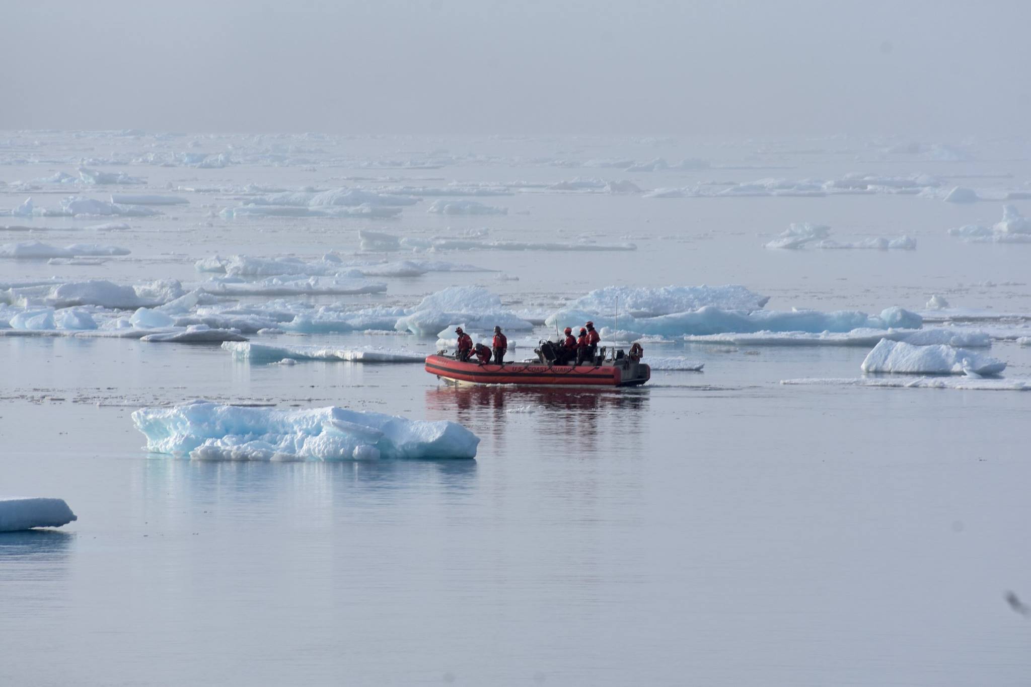 A small boat sails a team of researchers across the dark ocean, with floating ice in the background.